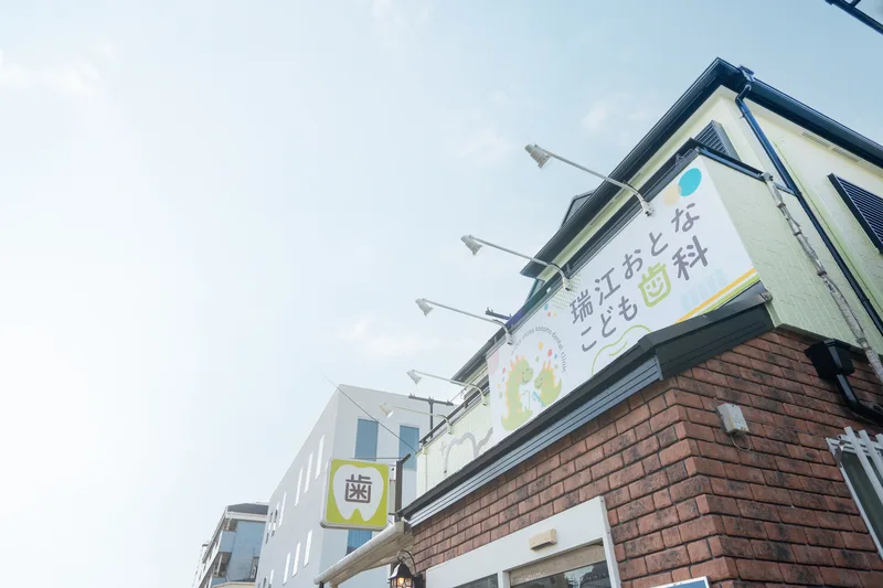 「歯」の突き出し看板と医院名の看板を掲げた外観を見上げた様子