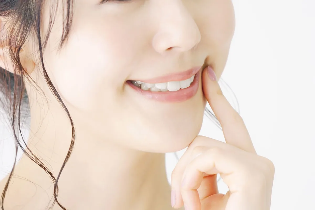 白い歯が見える笑顔の口元に指を添えた女性