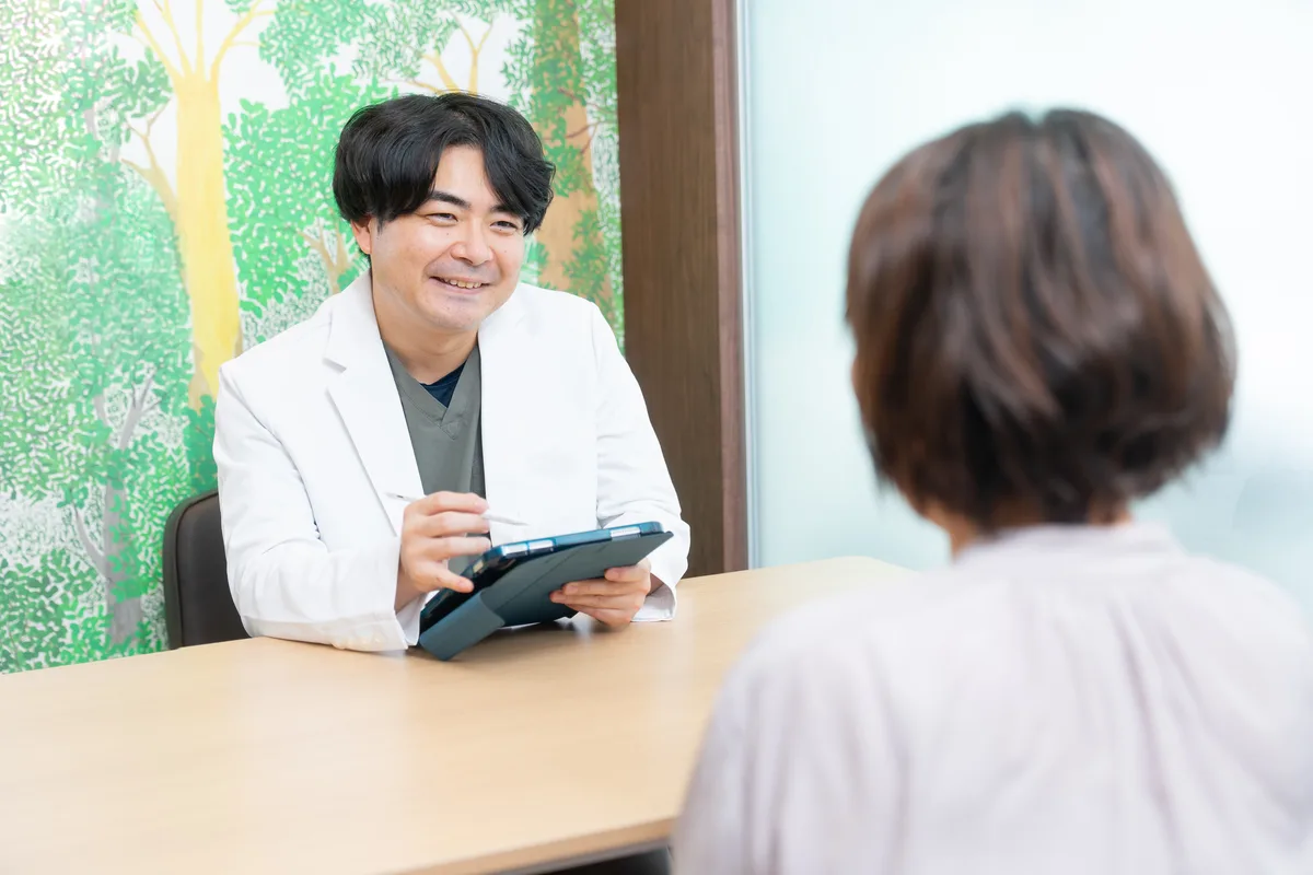 白衣の歯科医師がタブレットを手に患者さんと話す様子