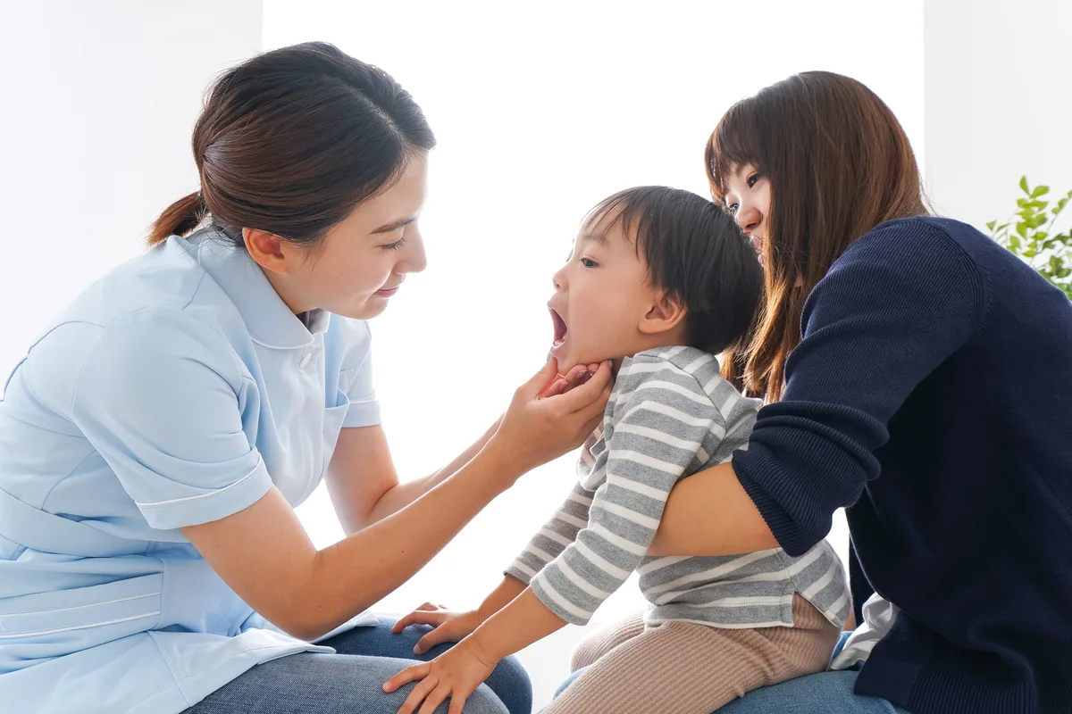 母親に抱かれた男の子の口を、女性スタッフが開けて見ている様子