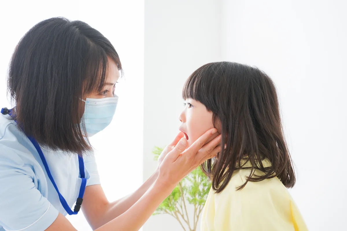 マスクをした女性スタッフが女の子のあごに手を添えて口の中を見る様子