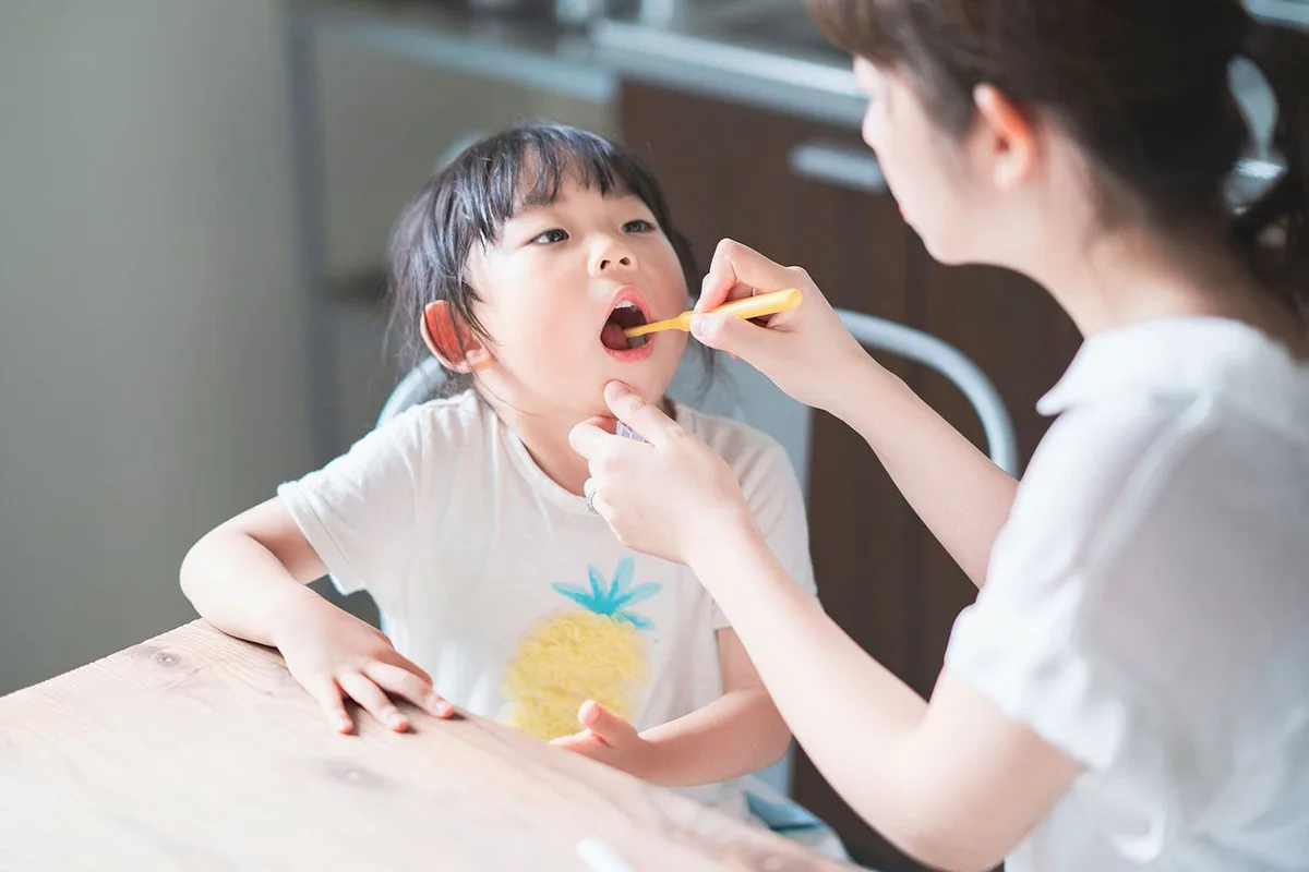 自宅の食卓で母親が子どもの歯を仕上げ磨きしている様子
