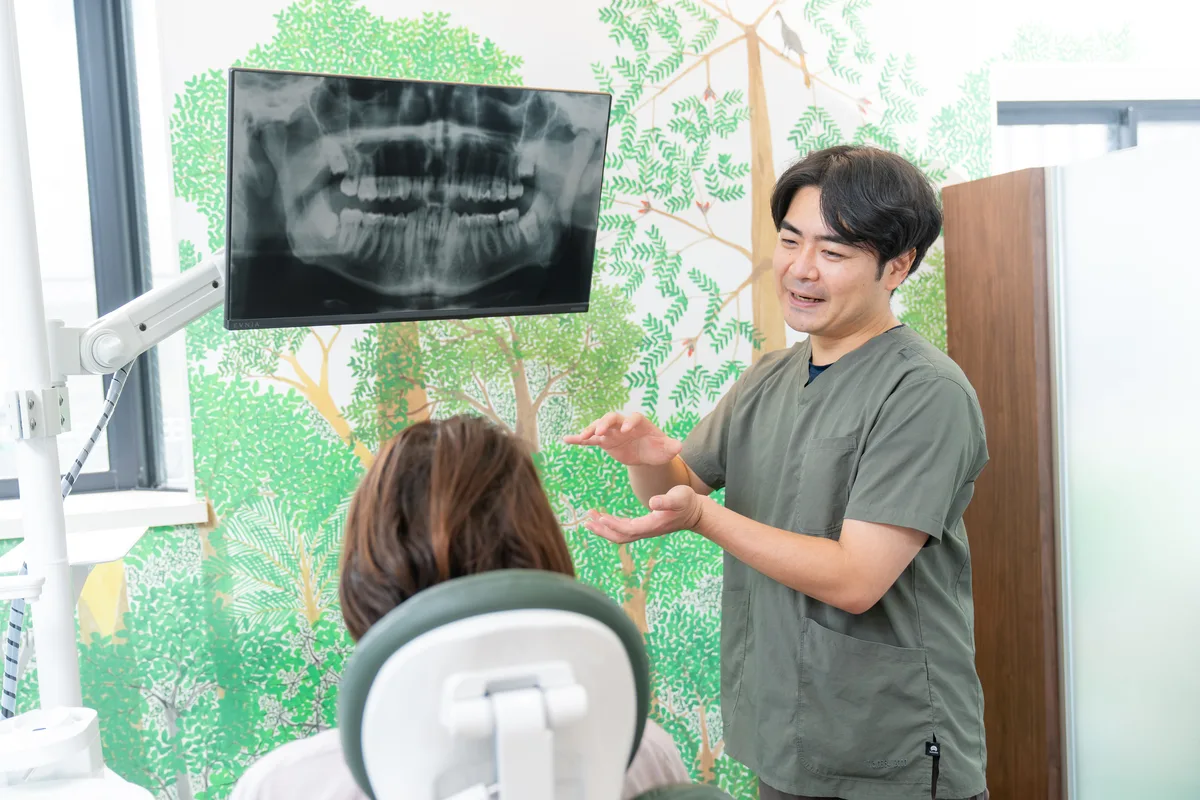 歯のレントゲン画像をモニターに映し、両手で示しながら説明する歯科医師