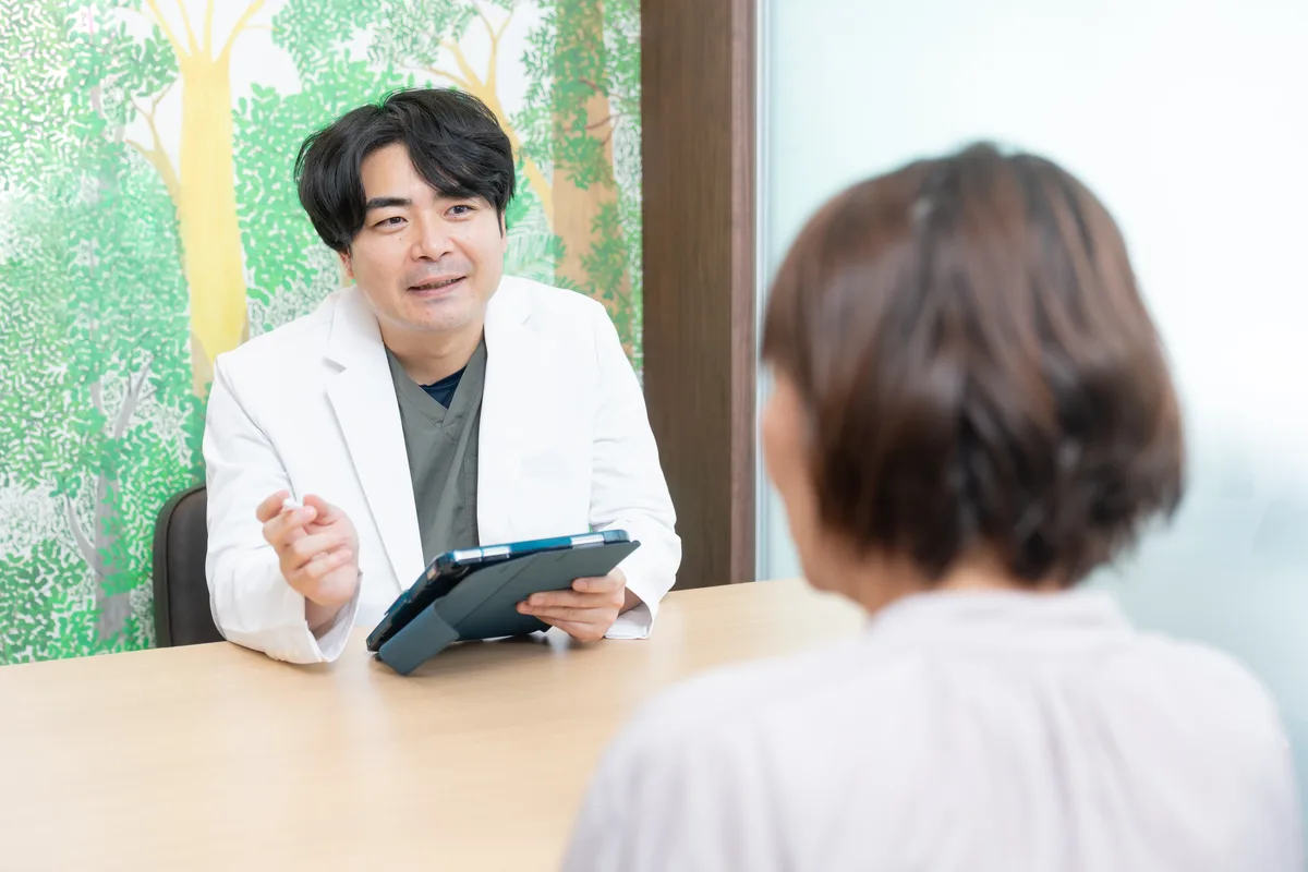 白衣の歯科医師がタブレットを手に患者さんと向き合って話す様子