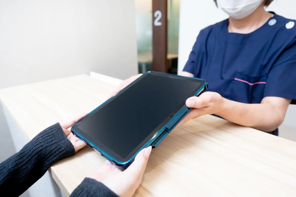 受付カウンター越しにスタッフとタブレットを受け渡す手元